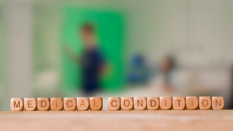 Medical-Concept-With-Wooden-Letter-Cubes-Or-Dice-Spelling-Medical-Condition-Against-Background-Of-Nurse-Talking-To-Patient-In-Hospital-Bed