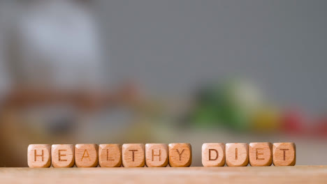 Medical-Concept-With-Wooden-Letter-Cubes-Or-Dice-Spelling-Healthy-Diet-Against-Background-Of-Woman-Chopping-Ingredients