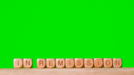 Medical-Concept-With-Wooden-Letter-Cubes-Or-Dice-Spelling-In-Remission-Against-Green-Screen-Background