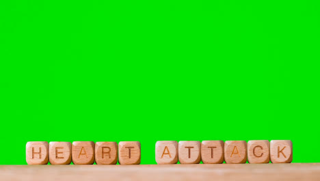 Medical-Concept-With-Wooden-Letter-Cubes-Or-Dice-Spelling-Heart-Attack-Against-Green-Screen-Background