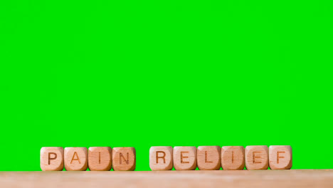 Medical-Concept-With-Wooden-Letter-Cubes-Or-Dice-Spelling-Pain-Relief-Against-Green-Screen
