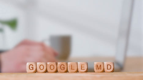 Concepto-Médico-Con-Cubos-De-Letras-De-Madera-O-Dados-De-Ortografía-Google-Md-Contra-El-Fondo-Del-Hombre-Mirando-La-Computadora-Portátil