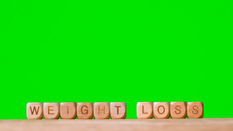 Medical-Concept-With-Wooden-Letter-Cubes-Or-Dice-Spelling-Weight-Loss-Against-Green-Screen-Background