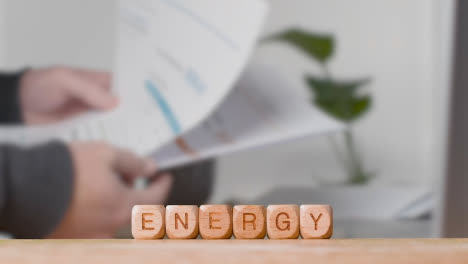 Concept-With-Wooden-Letter-Cubes-Or-Dice-Spelling-Energy-Against-Background-Of-Person-Looking-At-Bills