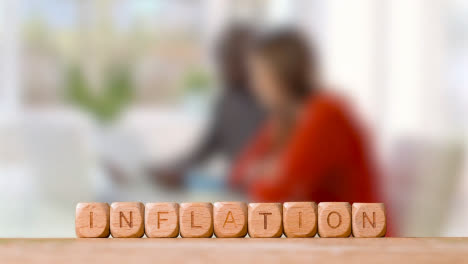 Concept-With-Wooden-Letter-Cubes-Or-Dice-Spelling-Inflation-Against-Background-Of-Couple-Looking-At-Bills