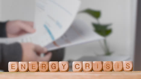 Concept-With-Wooden-Letter-Cubes-Or-Dice-Spelling-Energy-Crisis-Against-Background-Of-Person-Looking-At-Bills