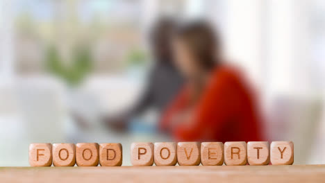 Concept-With-Wooden-Letter-Cubes-Or-Dice-Spelling-Food-Poverty-Against-Background-Of-Couple-Looking-At-Bills