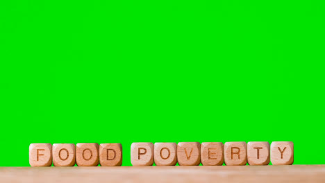 Concept-With-Wooden-Letter-Cubes-Or-Dice-Spelling-Food-Poverty-Against-Green-Screen-Background
