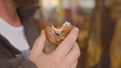 Cerca-De-Hombre-Comiendo-Huevo-Escocés-De-Puesto-De-Comida-Para-Llevar-En-El-Mercado-De-Borough,-Londres,-Gran-Bretaña.