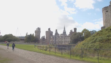 Person-Walking-By-Castle-Walls-In-Bute-Park-In-Cardiff-Wales-With-City-Skyline-And-Principality-Stadium