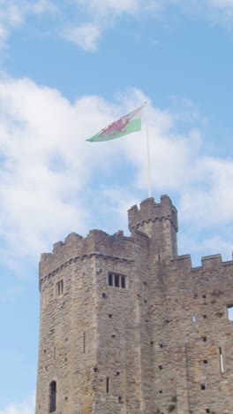 Vertical-Video-Of-Welsh-Flag-Flying-From-Cardiff-Castle-Against-Blue-Sky