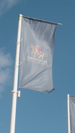 Vertical-Video-Of-Promotional-Flags-Flying-From-Cardiff-Castle-Against-Blue-Sky