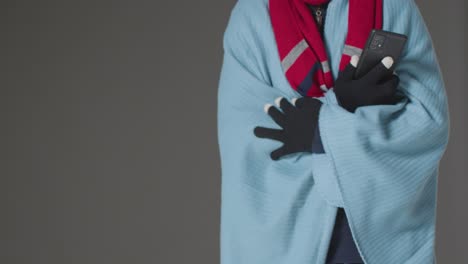 Close-Up-Of-Person-Wearing-Blanket-And-Gloves-Using-Mobile-Phone-Trying-To-Keep-Warm-In-Energy-Crisis-1