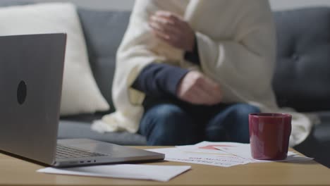 Person,-Die-Zu-Hause-Eine-Decke-Trägt-Und-Versucht,-Sich-Mit-Laptop-Und-Rechnungen-Warm-Zu-Halten