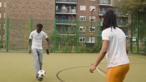 Künstlicher-Fußballplatz-Im-Städtischen-Stadtgebiet-Mit-Jungem-Paar,-Das-Fußball-Tritt-6