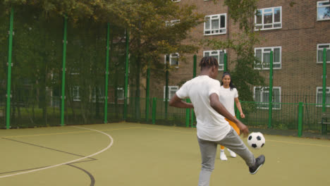 Nahaufnahme-Eines-Künstlichen-Fußballplatzes-Im-Städtischen-Stadtgebiet-Mit-Jungem-Paar,-Das-Fußball-1-Tritt