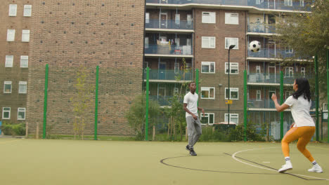 Nahaufnahme-Eines-Künstlichen-Fußballplatzes-Im-Städtischen-Stadtgebiet-Mit-Jungem-Paar,-Das-Fußball-2-Tritt