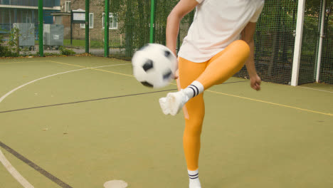 Young-Couple-Kicking-Football-On-Artificial-Soccer-Pitch-In-Urban-City-Area