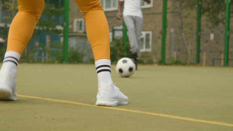 Nahaufnahme-Einer-Frau,-Die-Auf-Einem-Künstlichen-Fußballplatz-Im-Städtischen-Stadtgebiet-Fußball-An-Einem-Mann-Vorbeidribbelt