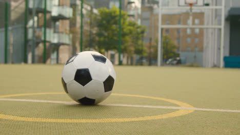 View-Of-Football-On-Centre-Circle-On-Empty-Artificial-Soccer-Pitch-In-Urban-City-Area-