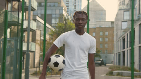 Portrait-Of-Young-Man-With-Football-Under-Arm-On-Artificial-Soccer-Pitch-In-Urban-City-Area-2