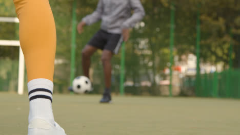 Close-Up-Of-Young-Couple-Kicking-And-Passing-Football-On-Artificial-Soccer-Pitch-In-Urban-City-Area-