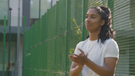 Female-Trainer-Encouraging-Male-Football-Player-On-Artificial-Soccer-Pitch-In-Urban-City-Area-1