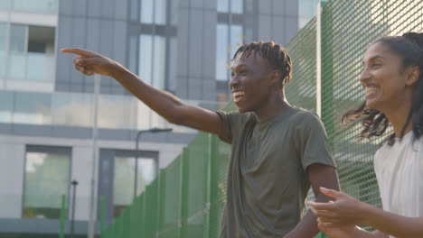 Supporters-Shouting-Encouragement-To-Football-Players-On-Artificial-Soccer-Pitch-In-Urban-City-Area-1