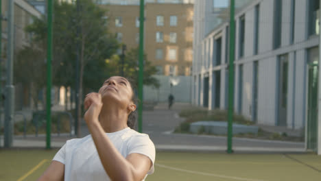 Female-Football-Player-Practising-Ball-Control-Heading-Soccer-Ball-On-Artificial-Soccer-Pitch-In-Urban-City-Area