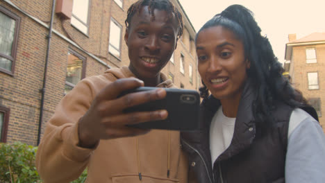 Close-Up-Of-Young-Couple-Watching-Sport-On-Mobile-Phone-In-Urban-City-Area-