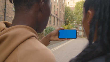 Close-Up-Of-Young-Couple-Watching-Sport-On-Blue-Screen-Mobile-Phone-In-Urban-City-Area-