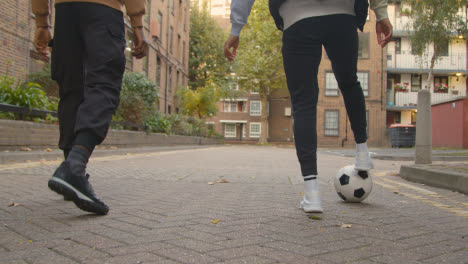 Nahaufnahme-Eines-Jungen-Paares,-Das-Fußball-Tritt-Und-Vorbeiführt,-Während-Er-Auf-Der-Straße-Im-Städtischen-Stadtgebiet-Spazieren-Geht