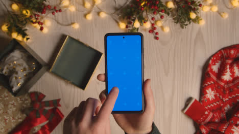 Overhead-Shot-Of-Person-Holding-Blue-Screen-Mobile-Phone-With-Christmas-Decorations-And-Wrapping-1