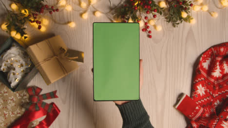 Overhead-Shot-Of-Person-Holding-Green-Screen-Digital-Tablet-With-Christmas-Decorations-And-Wrapping