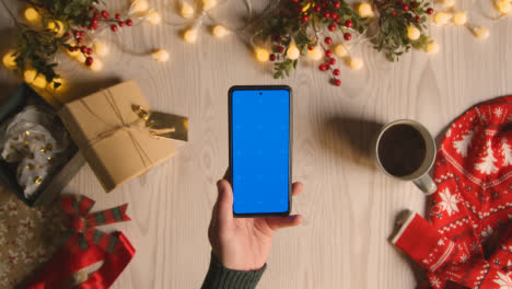 Overhead-Shot-Of-Person-Holding-Blue-Screen-Mobile-Phone-With-Christmas-Decorations-And-Wrapping-2