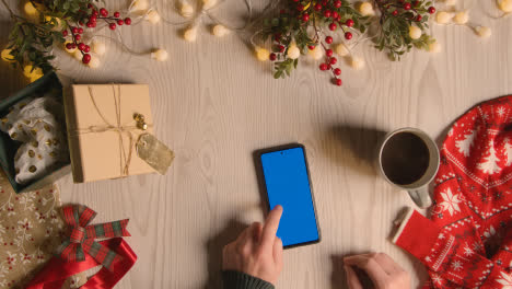 Overhead-Shot-Of-Person-Holding-Blue-Screen-Mobile-Phone-With-Christmas-Decorations-And-Wrapping-3