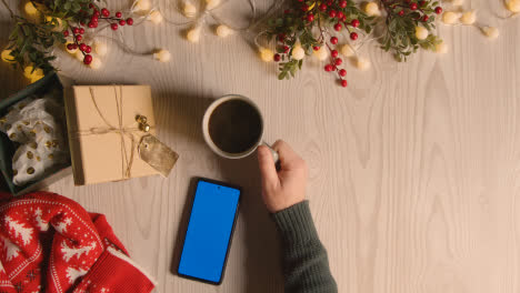 Overhead-Shot-Of-Person-Holding-Blue-Screen-Mobile-Phone-With-Christmas-Decorations-And-Wrapping-4