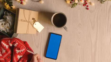 Overhead-Shot-Of-Person-Holding-Blue-Screen-Mobile-Phone-With-Christmas-Decorations-And-Wrapping-5