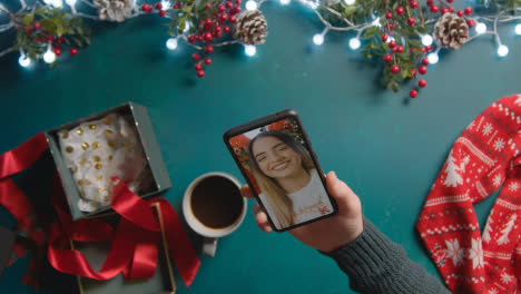 Overhead-Shot-Of-Person-Having-Christmas-Video-Call-With-Friend-On-Mobile-Phone-With-Christmas-Decorations-As-Background-2