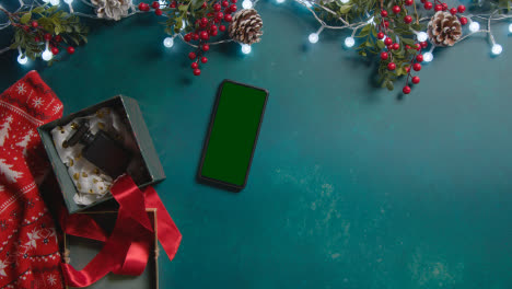 Overhead-Shot-Of-Person-With-Green-Screen-Mobile-Phone-With-Christmas-Decorations-And-Gifts-2