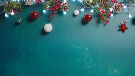 Overhead-Shot-Of-Christmas-Lights-With-Berries-And-Tree-Decorations-On-Green-Background