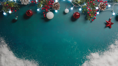 Overhead-Shot-Of-Christmas-Lights-With-Berries-And-Tree-Decorations-On-Green-Background-With-Snow