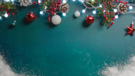 Defocused-Overhead-Shot-Of-Christmas-Lights-With-Berries-And-Tree-Decorations-On-Green-Background-With-Snow