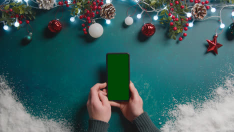Overhead-Aufnahme-Einer-Person,-Die-Ein-Greenscreen-Handy-über-Weihnachtsdekorationen-Hält