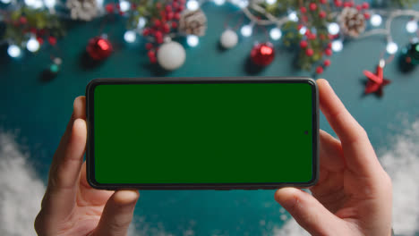 Fotografía-Cenital-De-Una-Persona-Que-Sostiene-Un-Teléfono-Móvil-Con-Pantalla-Verde-Sobre-Las-Decoraciones-Navideñas-1