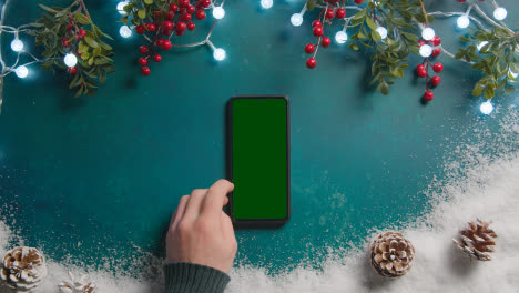 Overhead-Weihnachtshintergrund-Mit-Grünem-Bildschirm,-Handy,-Schnee,-Lichter,-Stechpalme-Und-Tannenzapfen