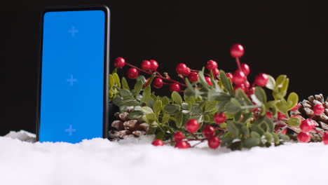 Handy-Mit-Blauem-Bildschirm-Auf-Weihnachtshintergrund-Mit-Schnee-Und-Laub-1