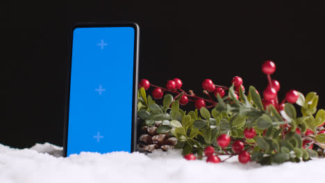 Handy-Mit-Blauem-Bildschirm-Auf-Weihnachtshintergrund-Mit-Schnee-Und-Laub-3