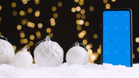 Handy-Mit-Blauem-Bildschirm-Auf-Weihnachtshintergrund-Mit-Schnee-Und-Baumschmuck-1