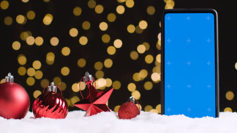 Handy-Mit-Blauem-Bildschirm-Auf-Weihnachtlichem-Hintergrund-Mit-Schnee-Und-Baumschmuck-2